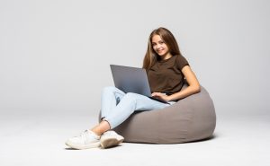 Happy young woman sitting on the floor using laptop on gray background